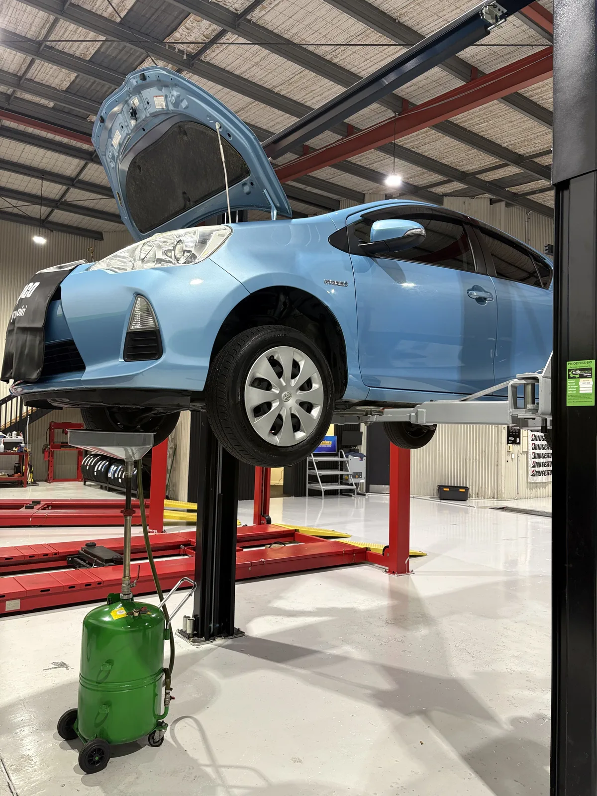 Toyota Aqua hybrid on the hoist above a mobile oil drain