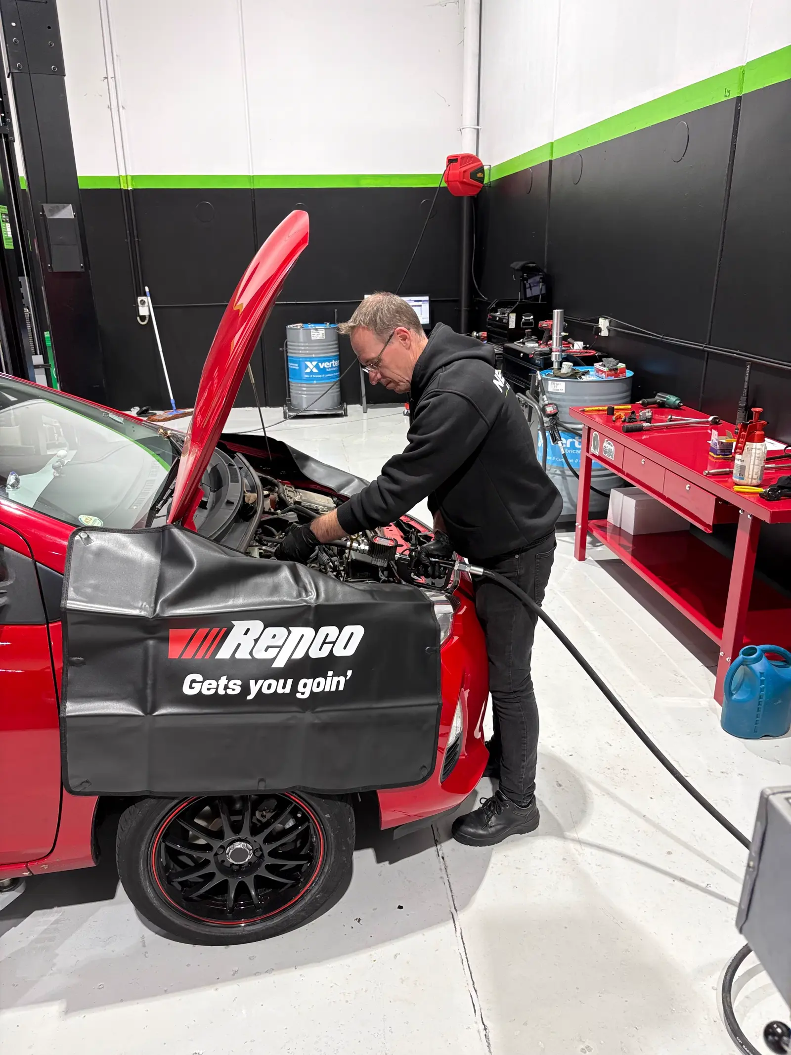 Technician servicing the engine bay of a red hatchback at NexGen Hamilton